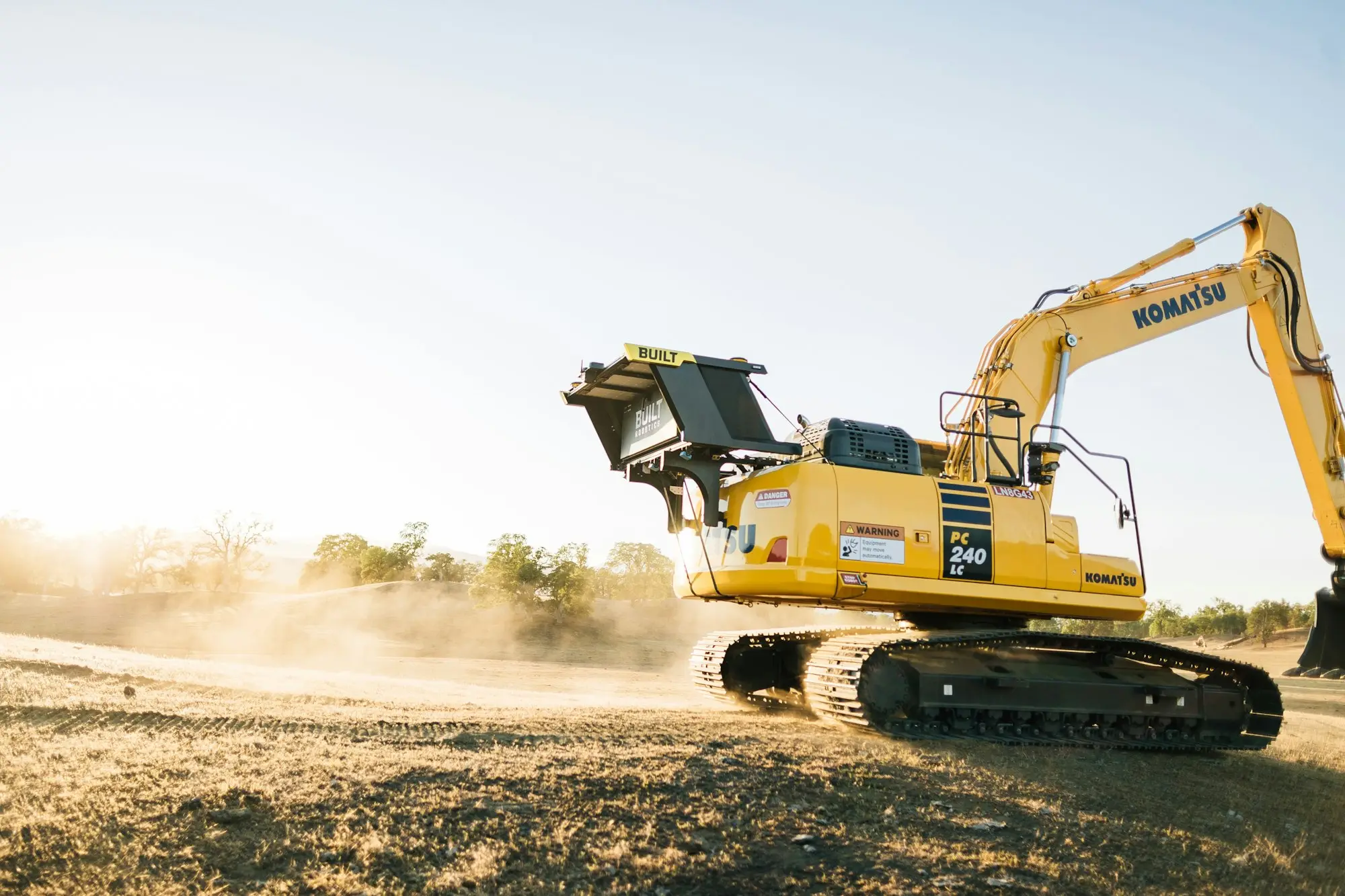Yellow excavator working a dusty cleared civil site in dry Australian bushland at golden hour