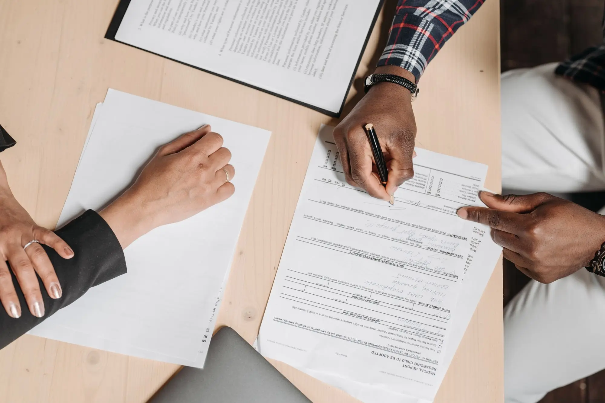 Overhead view of a business seller and buyer signing contract of sale paperwork at a timber desk